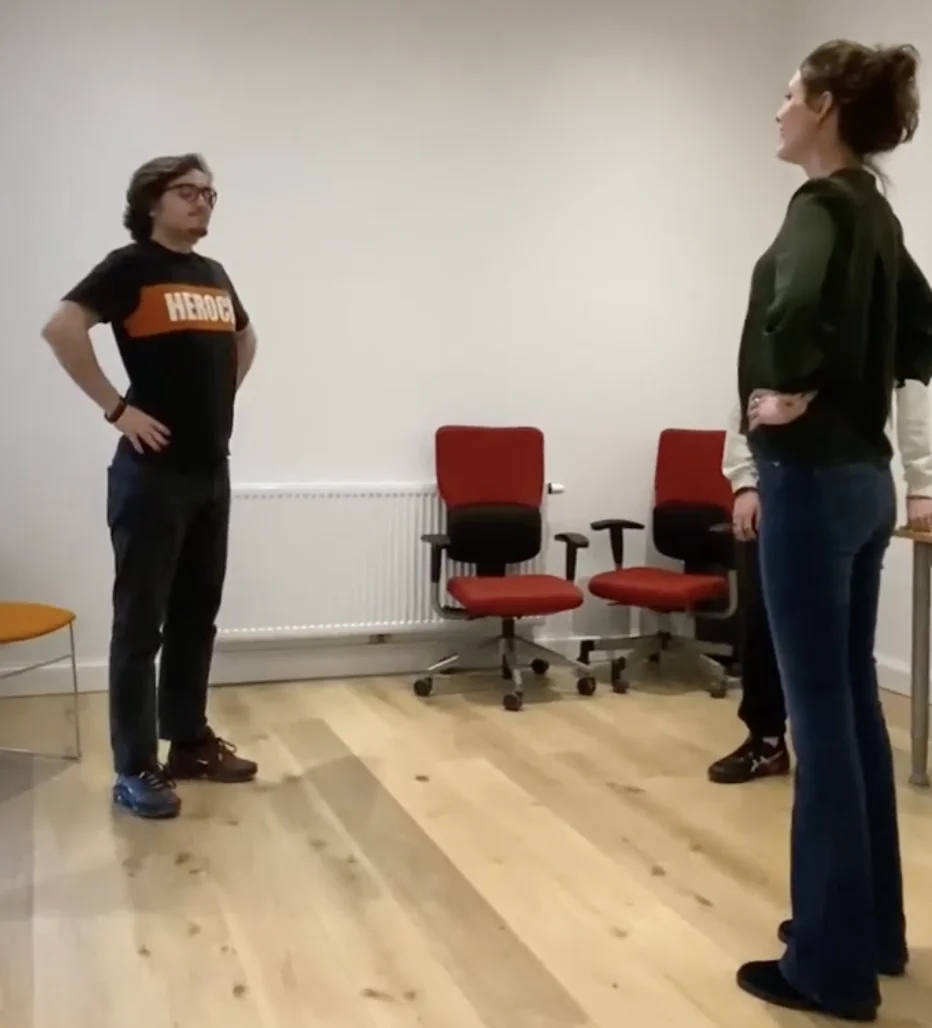 elevator-pitch. Un élève se tient debout, droit, les mains sur les hanches face à l'intervenante positionnée de la même manière.
