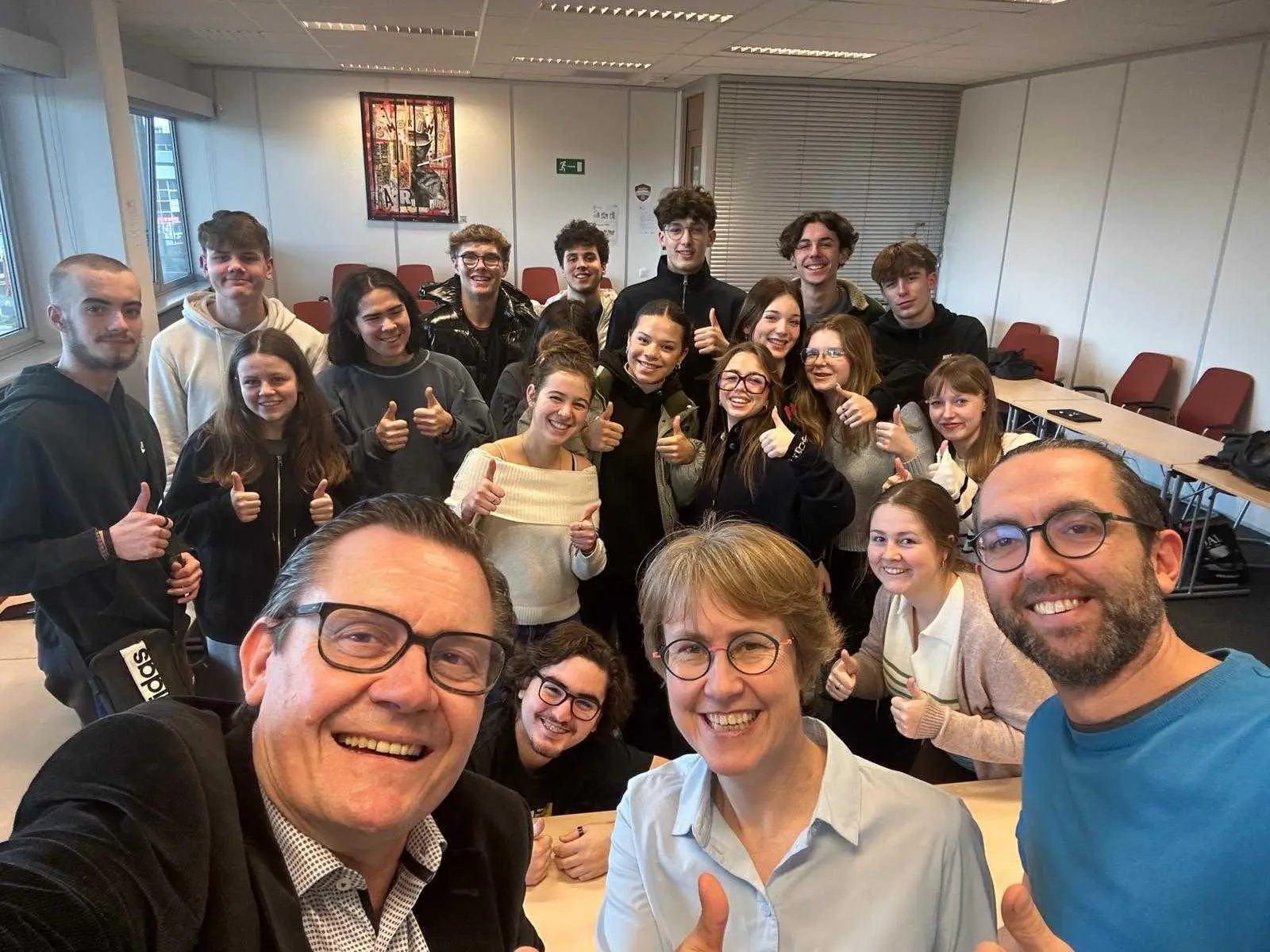Trois adultes au premier plan, les élèves derrière. Il s'agit d'un selfie de groupe pris dans une salle de classe.